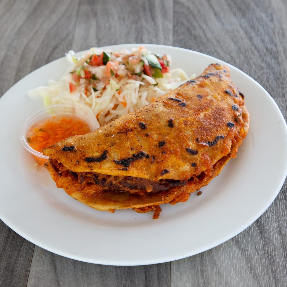 Grilled stuffed flatbread served with shredded cabbage salad, fresh salsa, and orange dipping sauce on a white plate.