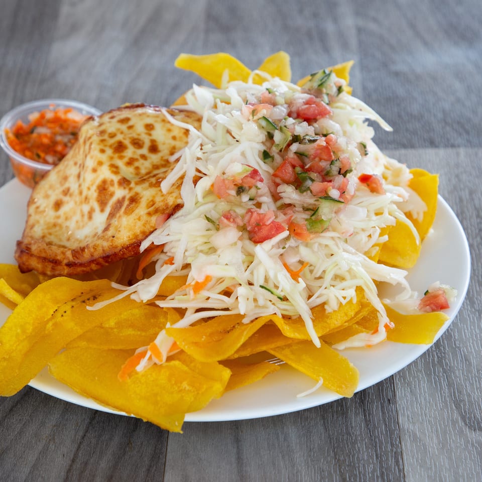 Plate of toasted stuffed arepas, fried plantain chips, shredded cabbage salad with pico de gallo, and dipping sauce.