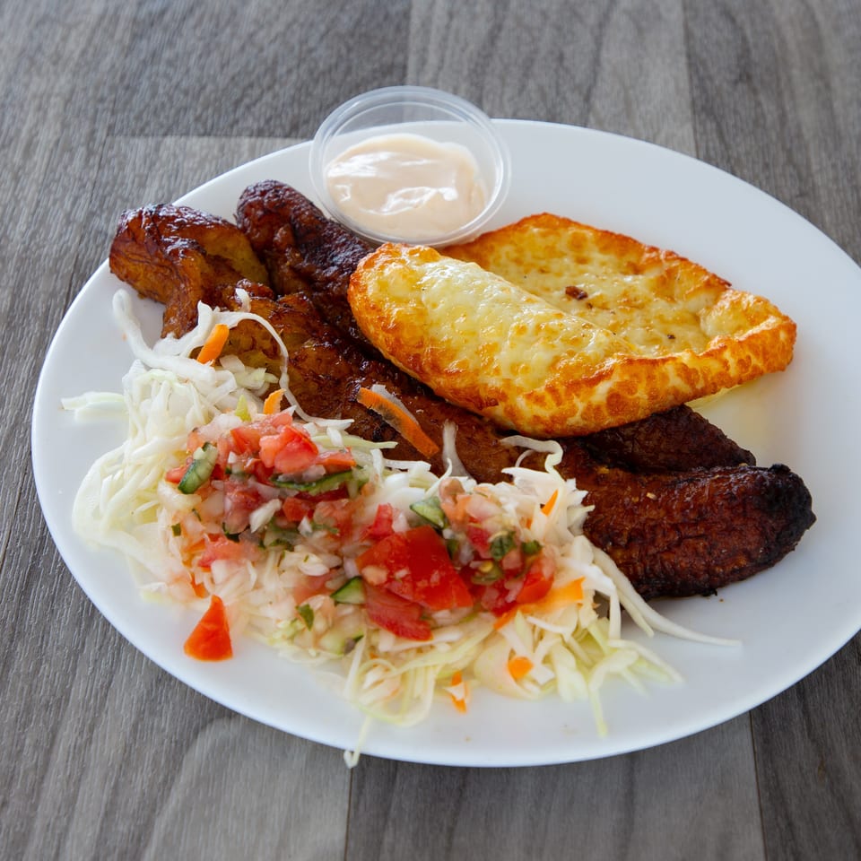 Platter of grilled meat, fried plantains, cheesy flatbread, cabbage slaw, fresh salsa, and creamy dipping sauce.