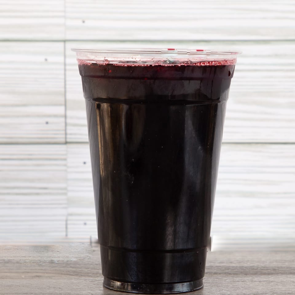 Black plastic cup filled with a dark red beverage on a wooden table against a white paneled wall.
